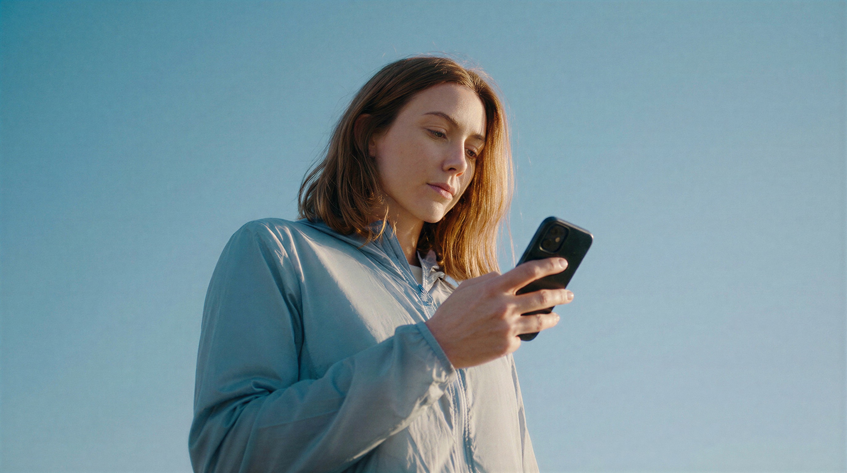 Kvinna som jämför priser i mobilen mot klarblå himmel